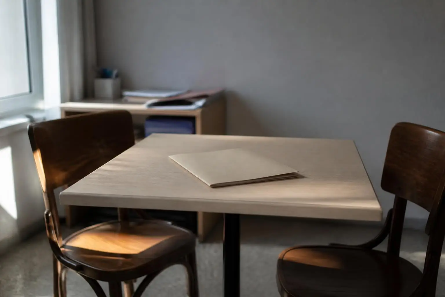 Deux chaises et une petite table de permanence, avec une chemise cartonnée fermée posée au milieu