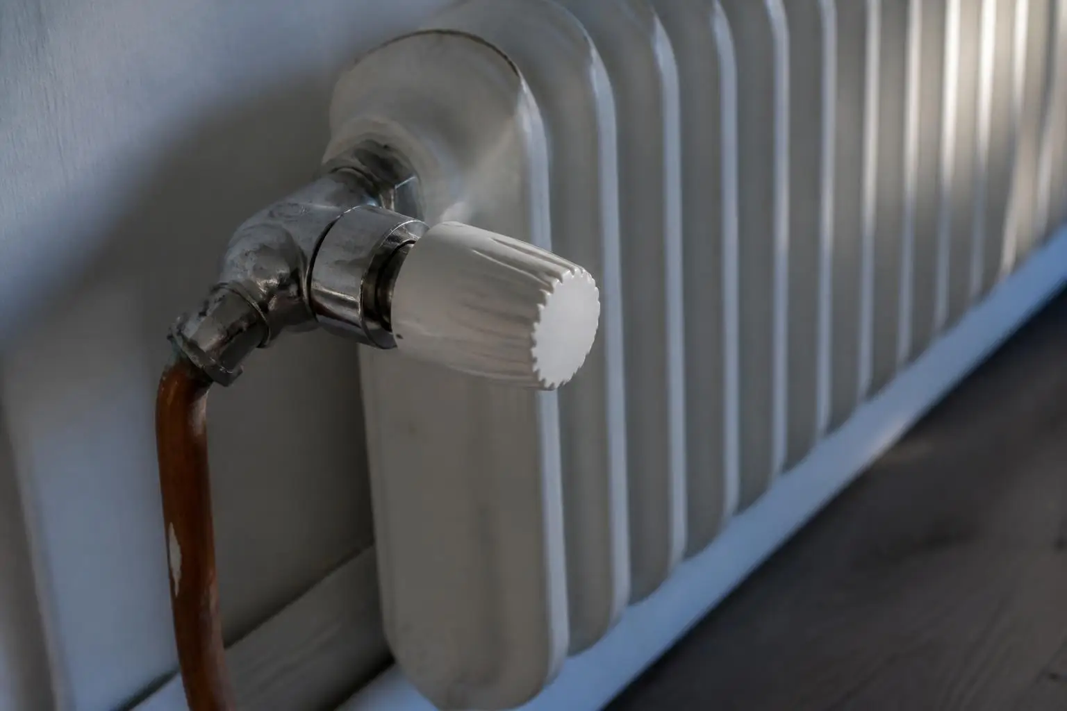 Robinet thermostatique de radiateur ouvert sur le cran 3, tuyau en cuivre et mur peint